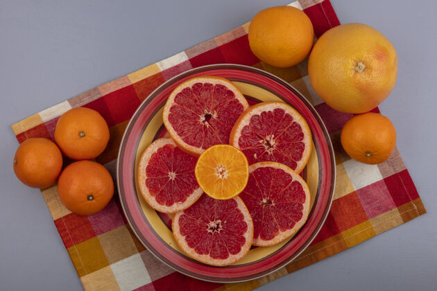 灰色上图：柚子片放在盘子里 橘子放在灰色背景的格子花纹的多色毛巾上橘子新鲜毛巾