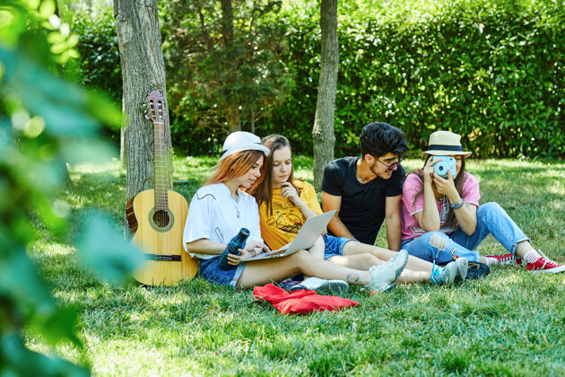 朋友四个年轻人在公园里玩 坐在草地上夏天团体人