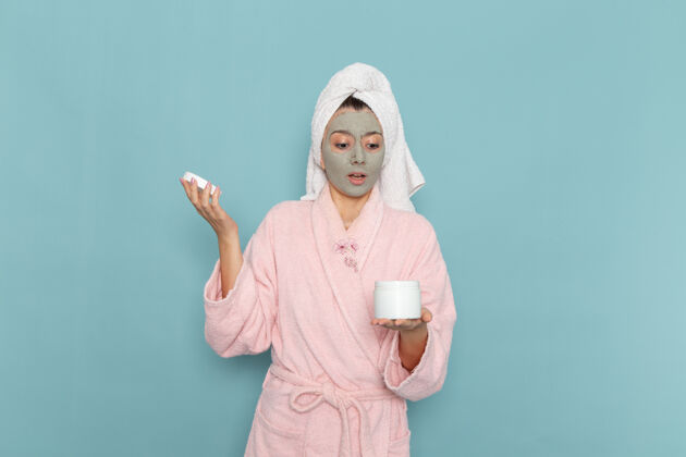 人正面图身着粉色浴袍的年轻女性淋浴后拿着面霜在蓝色墙壁上美丽的水浴面霜自护淋浴浴室人成人浴室