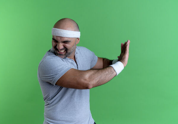男戴着头巾的成熟运动型男人站在绿色的墙壁上用厌恶的表情做着防卫的手势站厌恶成熟