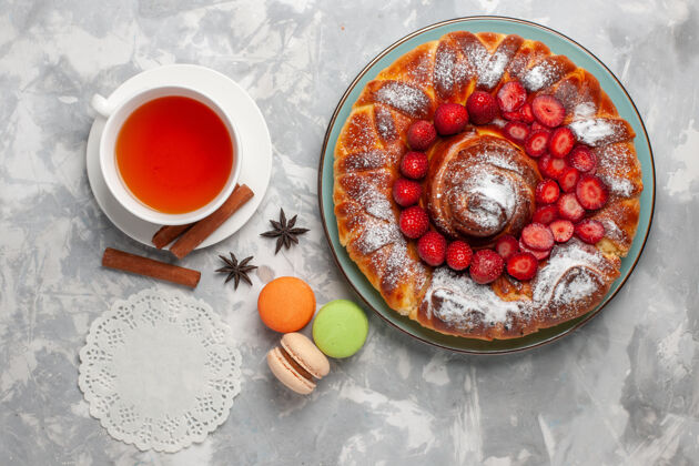 法式俯瞰美味的草莓派 配上法国马卡龙和一杯白桌子上的茶饼干糖蛋糕甜烤派杯子饼干碗