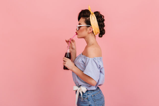 人美丽的黑发女人的侧视图穿着复古服装的可爱女孩喝饮料的摄影棚照片玩耍孤立的粉红色套装