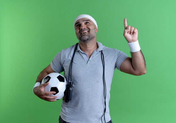 运动戴着头巾的成熟的运动型男人举着足球指着绿色的墙壁 有着新的想法足球运动员绳子