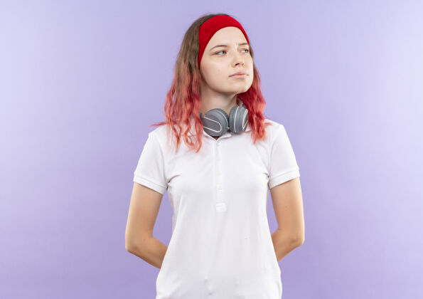 自信戴着耳机的年轻运动女郎站在紫色的墙上 带着自信的表情望向一边耳机女人人