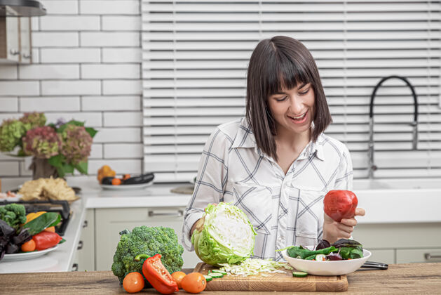 新鲜在现代厨房的背景下 漂亮的黑发女郎微笑着在沙拉上切蔬菜维生素厨房女人