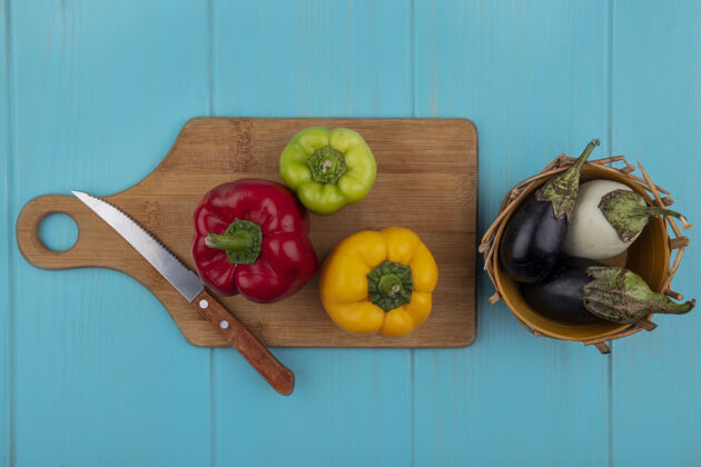 新鲜的顶视图彩色甜椒在一个菜板上用刀与白色和黑色茄子在一个蓝绿色的背景篮子铃铛刀胡椒