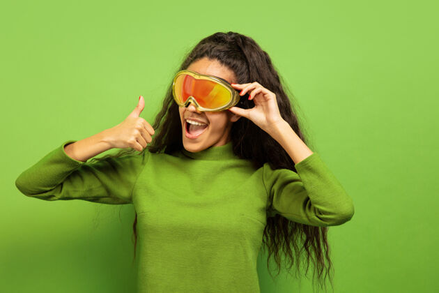 面具以绿色工作室为背景 黑色皮肤的非洲裔年轻女子的滑雪面具肖像人类情感的概念 面部表情 销售 广告 冬季运动和假日微笑 竖起大拇指人惊讶情感