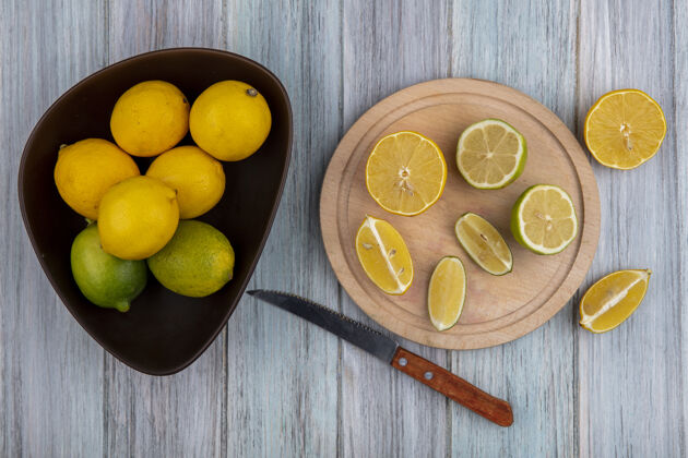 酸橙顶视图柠檬在碗和楔子在切菜板与刀在灰色背景上水果楔形切