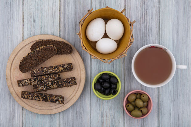 鸡蛋顶视图一杯茶 篮子里有鸡蛋 架子上有棕色面包片 灰色背景上有橄榄棕色顶杯子
