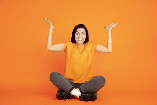 公司橙色工作室背景上的白种人年轻女子肖像穿着衬衫的漂亮黑发女性模特人类情感的概念 面部表情 销售 广告广告空间指向上工作女商人行政