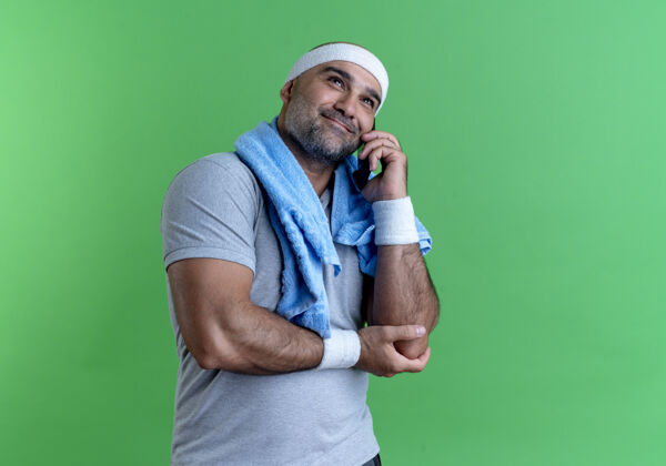 人戴着头巾 脖子上围着毛巾 脸上挂着微笑 站在绿色墙壁上讲手机的成熟运动型男人男人成熟谈话
