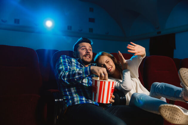女迷人的年轻白种人夫妇在电影院 房子或电影院看电影看起来富于表现力 惊讶和情绪化独自坐着玩关系 爱情 家庭 周末时间微笑观众害怕