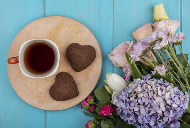 杯子一杯茶的顶视图在一个木制的厨房板与心形饼干与美妙的鲜花隔离在一个蓝色的木制背景木头视图心