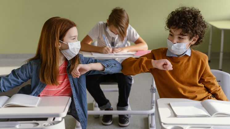 学校戴着医用面罩的孩子们在课堂上做肘部敬礼的正面图新常态水平学习