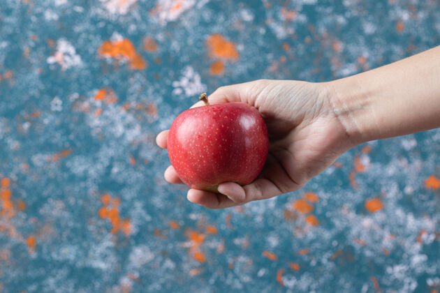季节手里拿着一个红苹果放在蓝色的表面上食物异国情调生物