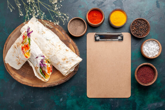 营养品俯瞰美味的肉三明治 用烤肉和调味料做成的 蓝色桌子上的记事本汉堡肉餐午餐三明治生的墨西哥煎饼记事本