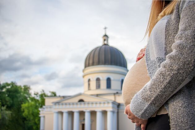 教怀孕的女人抱着她的肚子站在诞生的大教堂前女人孕妇手