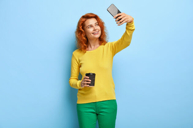 展示笑容可掬的姜女在现代手机上自拍上传到社交网络墙壁正片图片