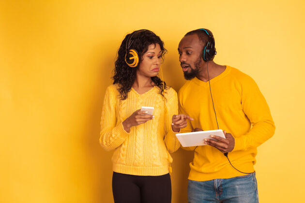 选择年轻感性的非裔美国人 穿着黄色背景的明亮休闲服美丽的情侣人类情感的概念 面部表情 关系 广告使用平板电脑和智能手机人衣服成人