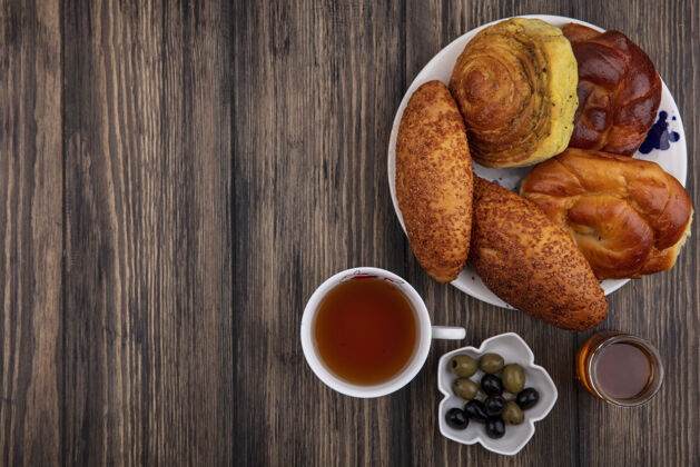 顶部盘子上的小面包顶视图 碗上放着橄榄和蜂蜜的茶 背景是木制的 有复印空间食物传统的橄榄