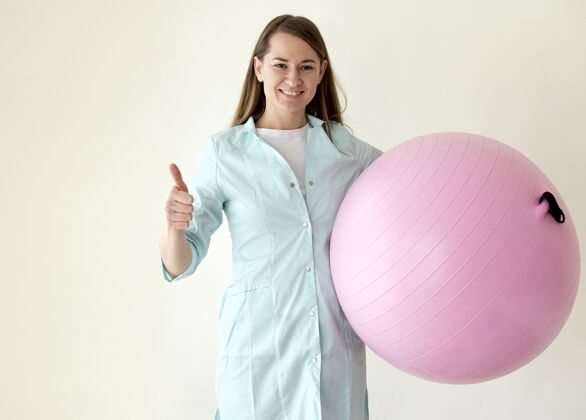 过程微笑的理疗师拿着健身球竖起大拇指活动紊乱健康