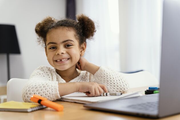 学习笑脸小女孩在家里的前视图在网上学校与笔记本电脑课程学校年轻
