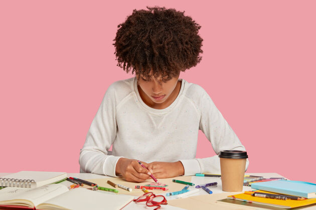 建筑师灵感迸发的黑人年轻女子喜欢用蜡笔在白纸上画画 注意力集中 有创造力的心情 创造一些原创的东西 独自坐在工作场所的粉色墙壁上个人设计师记事本