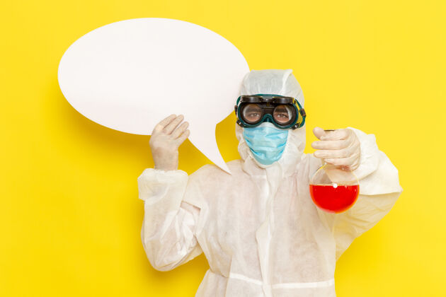 科学正面图穿着特殊防护服的男科学工作者拿着装有红色溶液的烧瓶 黄色桌子上有白色标志工人科学溶液