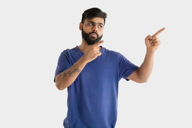 选择美丽的男性半身肖像隔离在白色的工作室背景年轻的情感印度教男子在蓝色衬衫面部表情 人类情感 广告概念指向和选择衬衫指向年轻