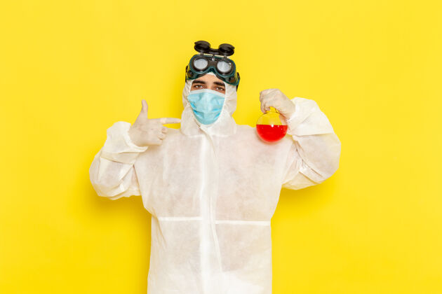 科学正面图穿着特殊防护服的男科学工作者拿着黄色表面上有红色溶液的烧瓶科学危险保护