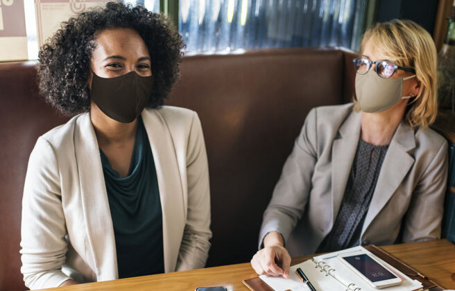冠状病毒午休时在咖啡馆戴口罩的女人商务女性朋友坐姿