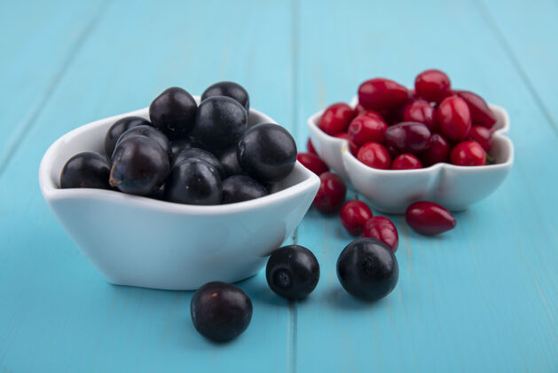 浆果侧视图新鲜的黑葡萄碗与山茱萸浆果在蓝色的木制背景新鲜木头蓝色