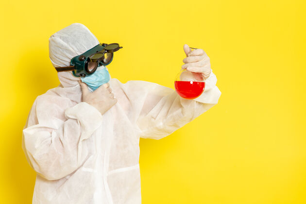 特殊正面图穿着特殊防护服的男科学工作者拿着黄色表面上有红色溶液的烧瓶思考科学医生专业