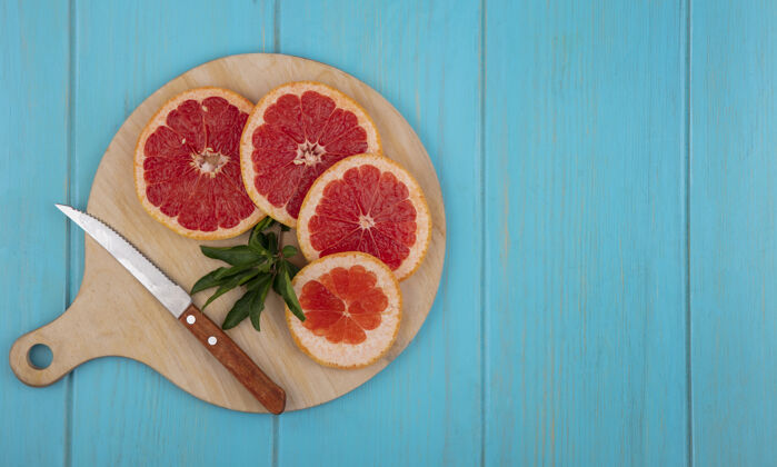 水果顶视图复制空间葡萄柚片在切割板上用刀在绿松石背景上复制切新鲜