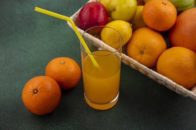 饮料侧视图橙汁与橙子柠檬和樱桃李子在一个绿色的背景篮子玻璃橙色玻璃柠檬