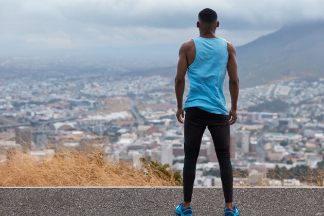 运动员人 自由 生活方式的概念穿着运动服的运动型男子的后视图 站在高高的道路上 从上面俯瞰美丽的城市景观与天空 蓝天和火山 火车运动外运动慢跑乡村