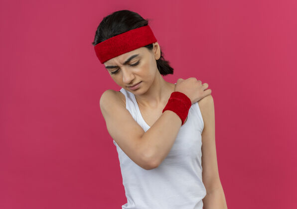 健身穿着运动服的年轻健身女 头箍贴着肩膀 站在粉色的墙上 看起来不舒服 感觉疼痛疼痛不适运动