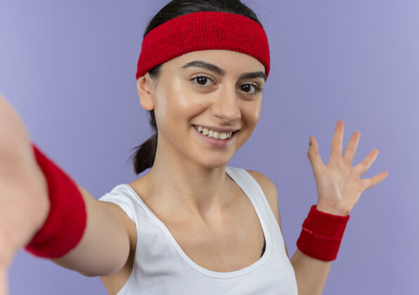 制造身穿运动服 头戴花边 手举紫色墙壁 微笑着表示欢迎的年轻健身女士运动装微笑站立
