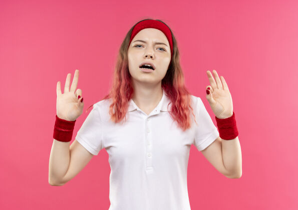 站立戴着头巾的年轻运动女性正在放松 做着冥想的姿势 手指站在粉色的墙上手势放松人