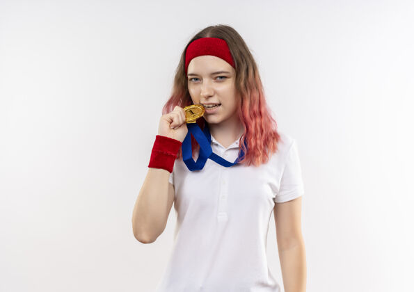 长相戴着头巾的年轻运动女性站在白墙上咬着金牌 看上去很自信咬站立金牌