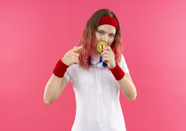 女性戴着头巾的年轻运动女性站在粉色的墙上 用手指着金牌 看上去很自信运动运动公民