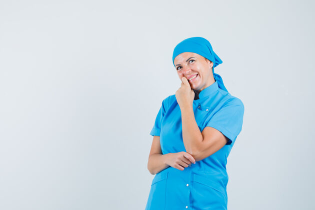 诊所女医生穿着蓝色制服站在思考的姿势 看起来很高兴 正面视图肖像治疗制服