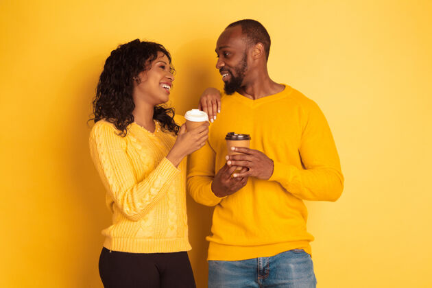 女性年轻感性的非裔美国人 穿着黄色背景的明亮休闲服美丽的情侣人类情感的概念 面部表情 关系 广告一起喝咖啡姿势化妆品夫妇