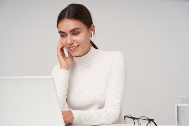 年轻快乐的年轻漂亮的黑发女人 扎着马尾辫 手放在键盘上 一边查看笔记本电脑上的邮箱 隔着白墙头发Mua黑发