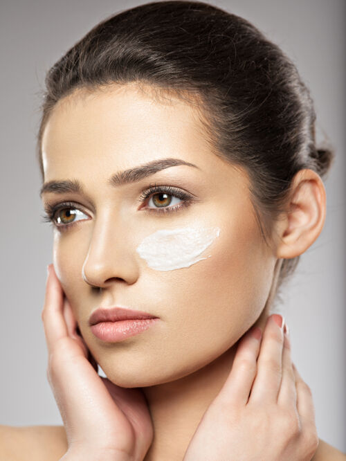 清洁年轻漂亮的女人用化妆霜涂抹在脸上靠近眼睛的地方护肤理念美容理念涂抹面霜护肤