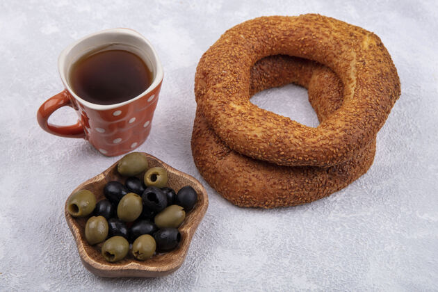 食物侧视图美味芝麻土耳其百吉饼与一杯茶和橄榄在一个白色背景的木碗杯子餐碗