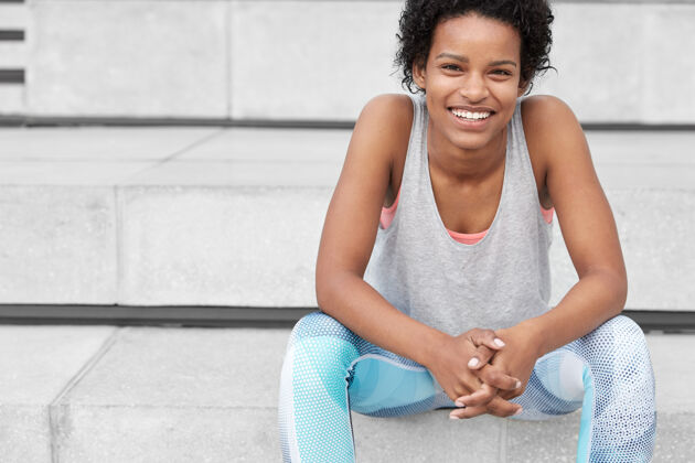 活力健康城市生活理念运动混血少女照片 皮肤黝黑 穿着运动服 有慢跑休息时间 坐在楼梯旁 有着牙齿般的微笑 在户外积极训练瘦身运动服青少年