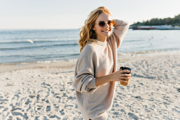 装备穿着毛衣的漂亮女人站在海边漂亮的金发女人在海边喝茶海边大海配件