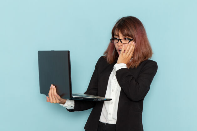 电脑前视图：穿着西装的女上班族在浅蓝色表面上使用笔记本电脑办公室笔记本电脑女业务员