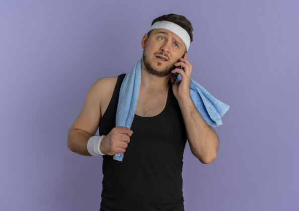 困惑戴着头巾 肩上扛着毛巾 站在紫色的墙上 一脸困惑地讲着手机的年轻健身男子头带移动小伙子